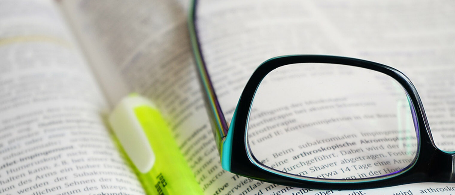 Brille und Stift liegen auf einem Buch