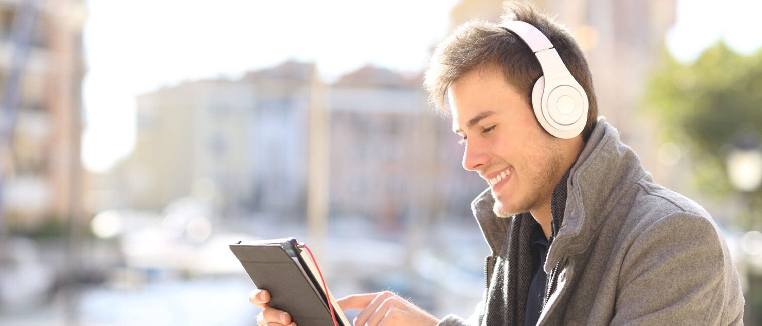 Junger Mann mit weißen Kopfhörern und Tablet in der Hand vor Häusern