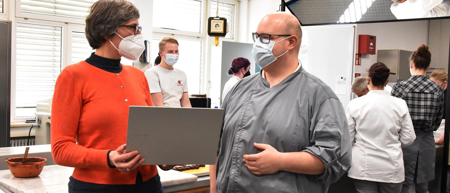 Maria Kreiner und Simon Rapp Maria Kreiner, Projektleiterin für digitales Lernen (links) im Gespräch mit Bäckermeister Simon Rapp (rechts) stehend mit Laptop.