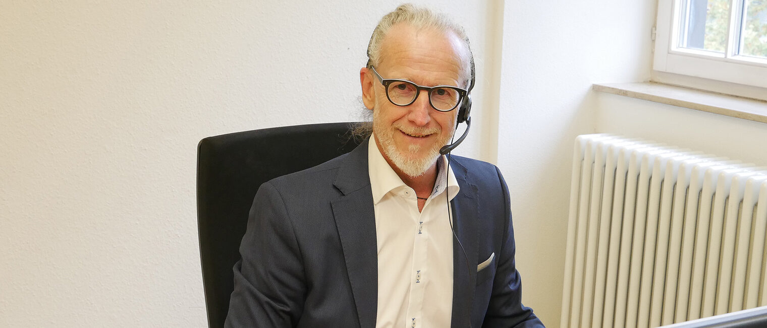 Thomas Thierolf, Dozent der Online-Akademie, sitzt mit Headset am Schreibtisch vor Computerbildschirm.