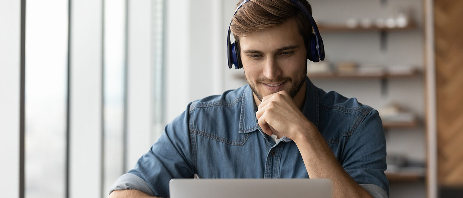 Junger Mann mit Headset schaut in Laptop-Bildschirm.