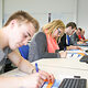 Auszubildende nehmen an einem Seminar teil und schreiben auf Arbeitsplätter, während sie vor Computern sitzen