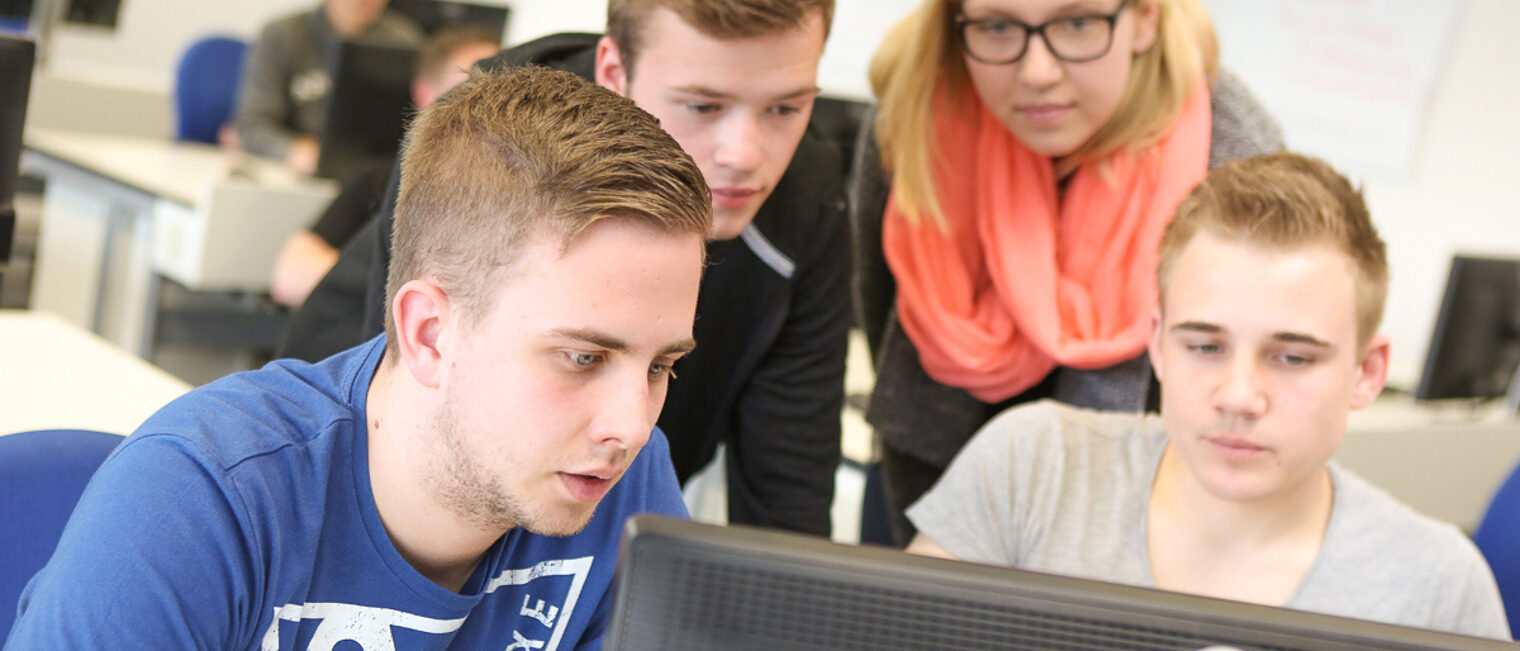 Seminarteilnehmende schauen auf einen Computermonitor Vier Auszubildende die an einem Kurs teilnehmen schauen auf ein Computerdisplay