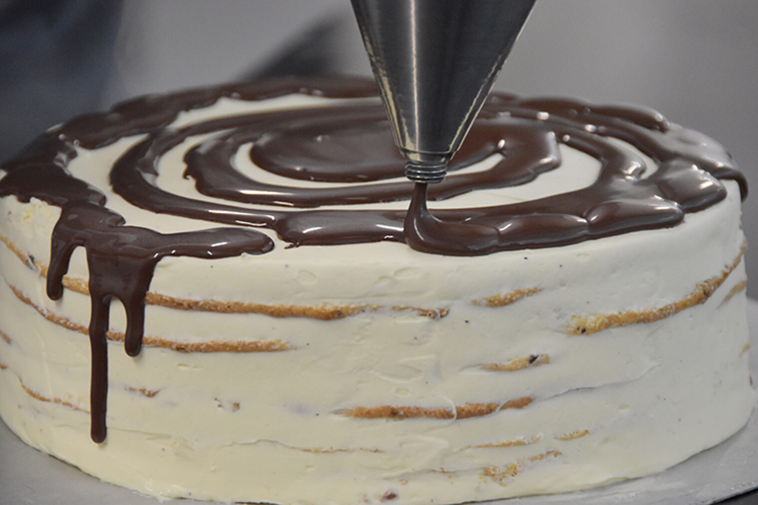 Nahaufnahme von Torte, die gerade mit Schokosauce verziert wird.