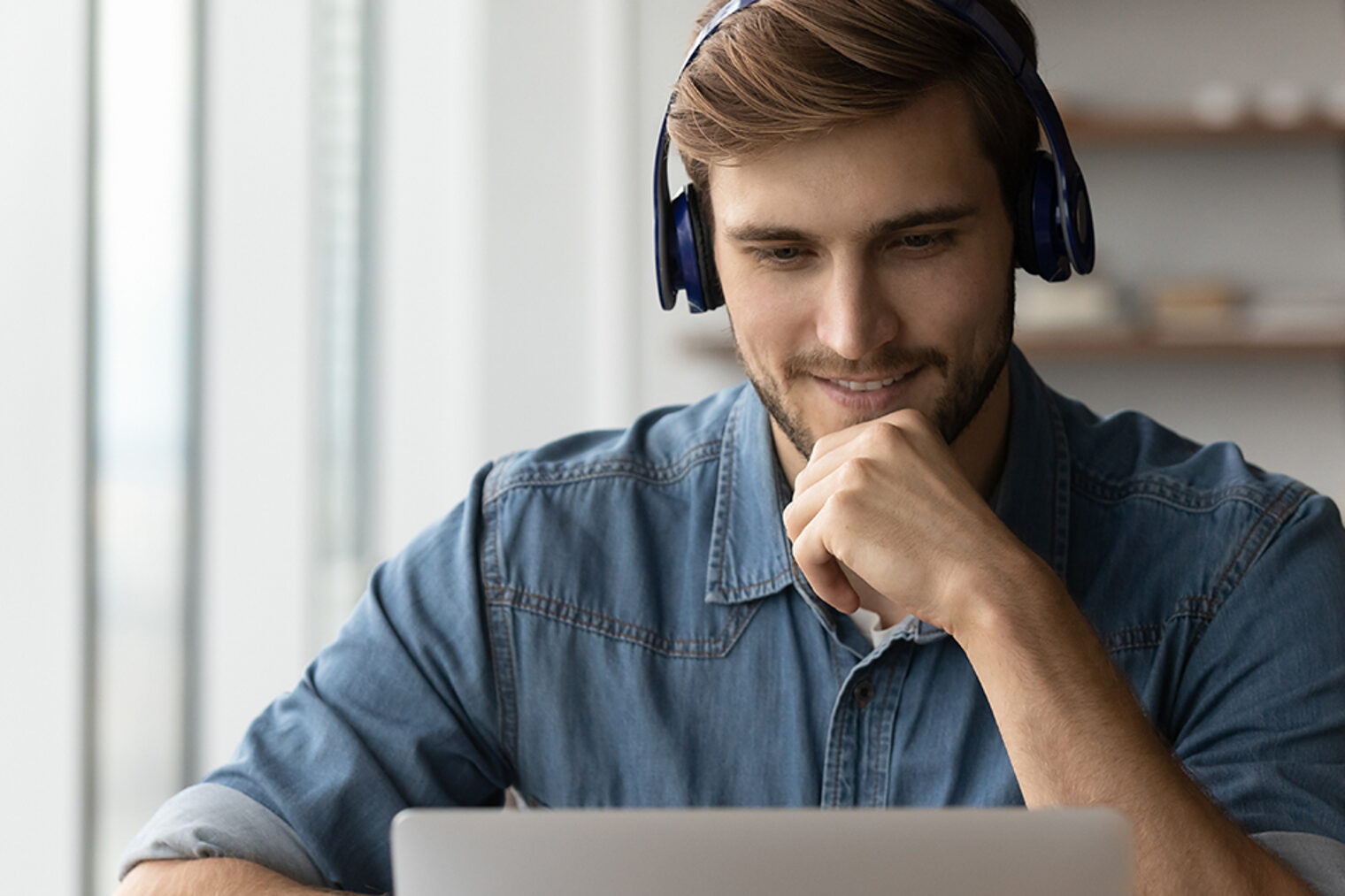 Junger Mann mit Headset schaut in Laptop-Bildschirm.