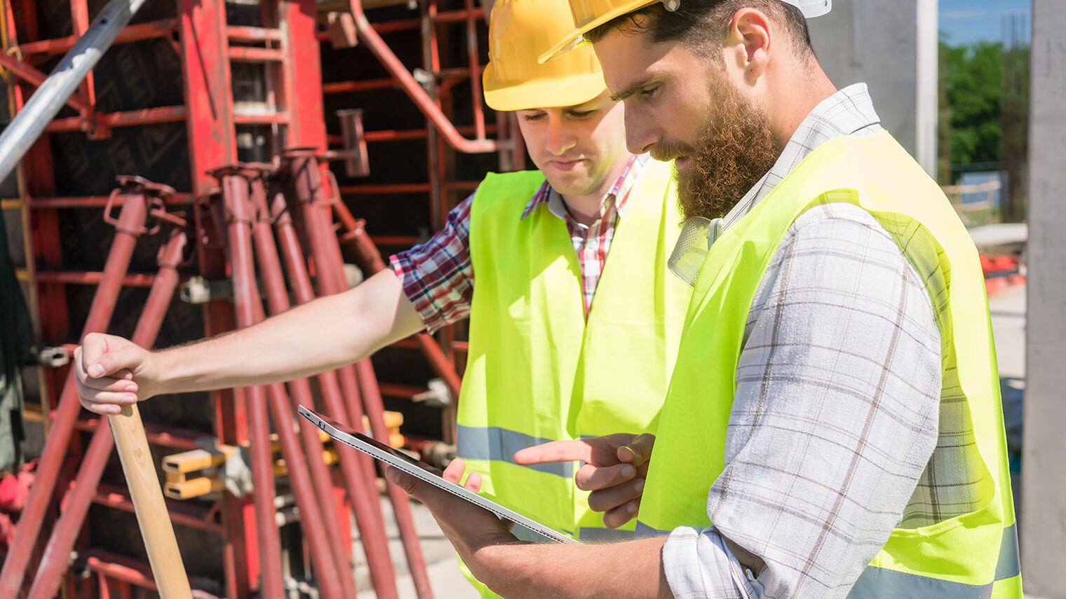 Zwei junge Bauarbeiter mit einem Tablet auf der Baustelle
