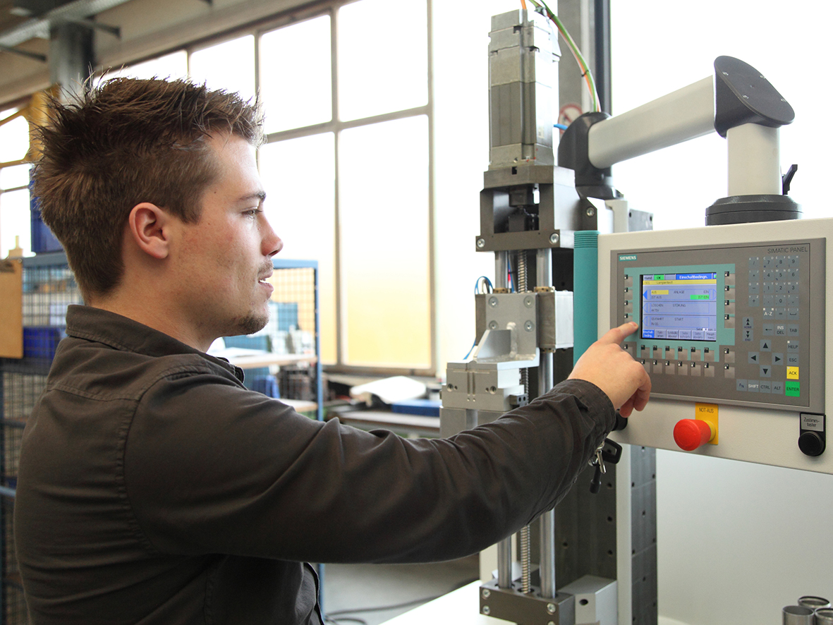 Feinwerkmechaniker tippt etwas in die Maschine ein.