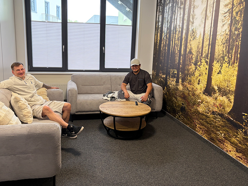 Azubi-Wohnheim in Waldshut: Aufenthaltsbereich mit zwei hellgrauen Sofas und Tapete mit Waldmotiv.